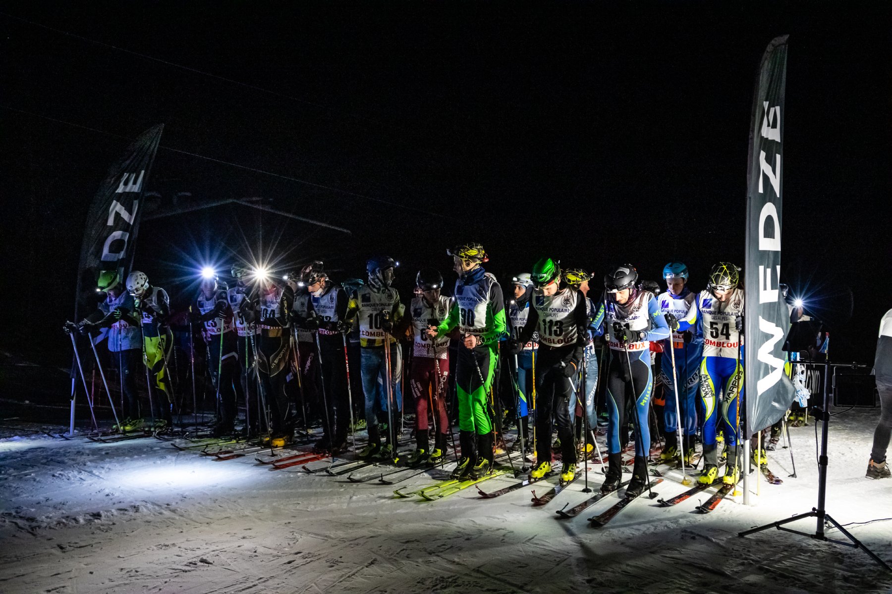 línea de salida desgarradora: esquiadores alineados por la noche, iluminación de faros