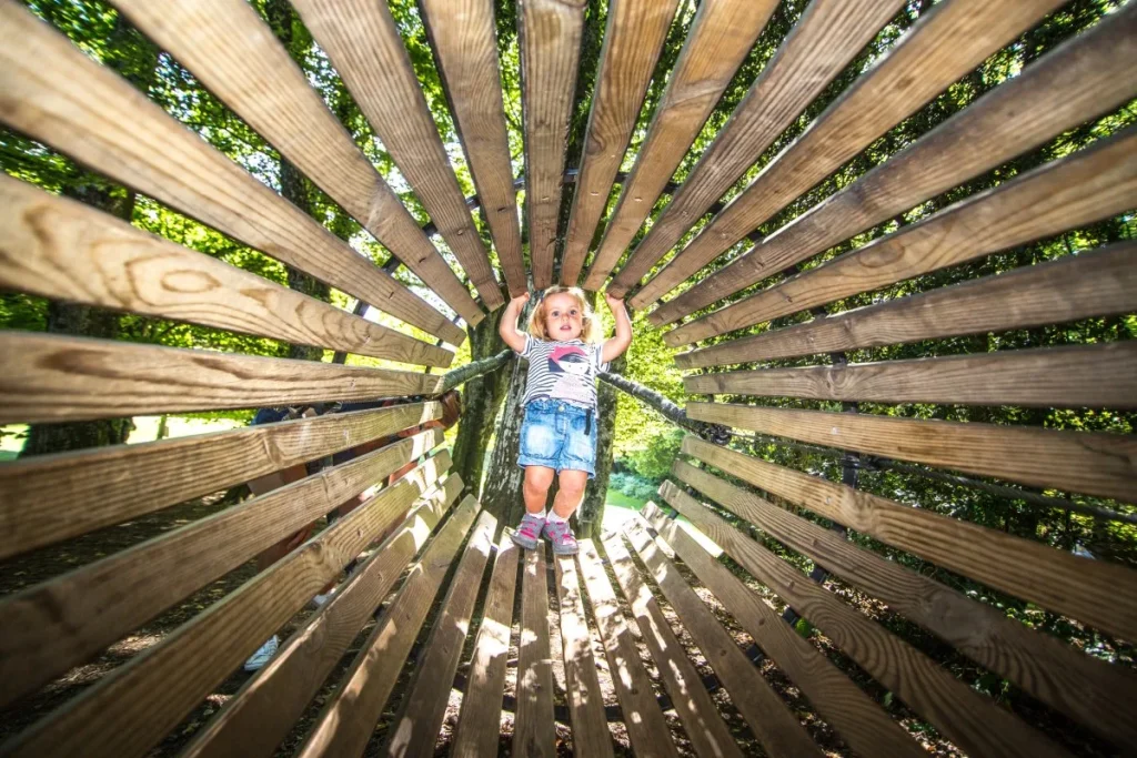 primer plano artístico niño jugando en estructura cónica de juegos de madera combloux