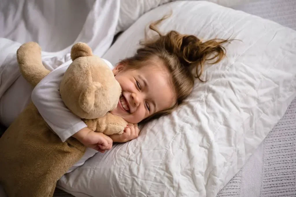 little girl lying in bed with child plush teddy bear
