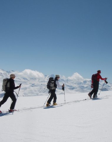 3 raquettistes file indienne dans paysages montagneux enneigés