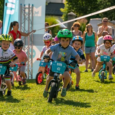 young children in full mountain bike race on field parents supporters